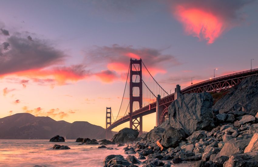 A wide shot of Golden Gate Bridge on the body of water near rock formations during sunset in San Francisco, California