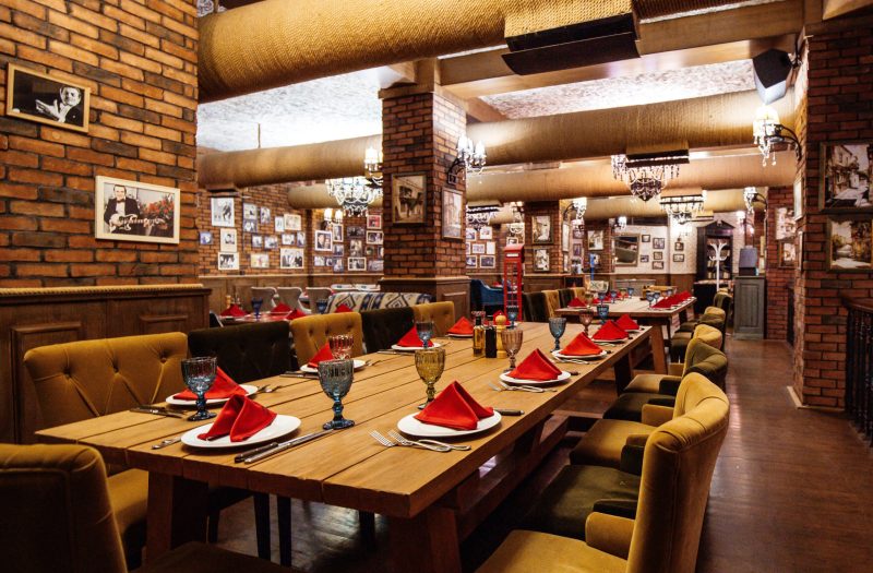 a restaurant hall with red brick walls wooden tables and pipes in the ceiling